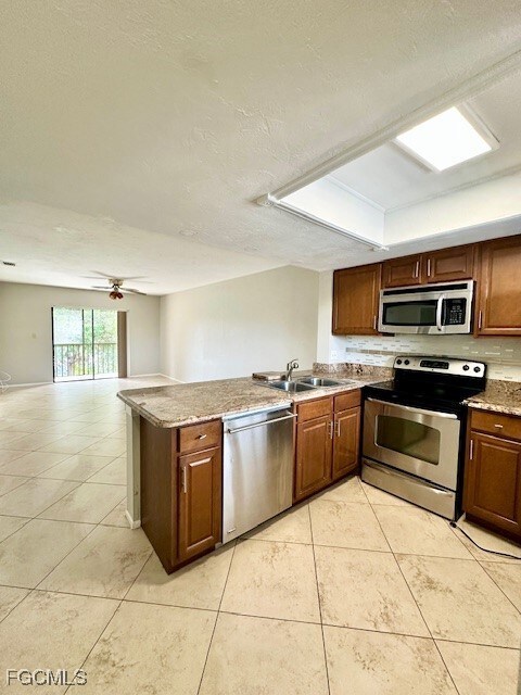 Kitchen featuring a textured ceiling, stainless steel appliances, a peninsula, light tile patterned flooring, and open floor plan