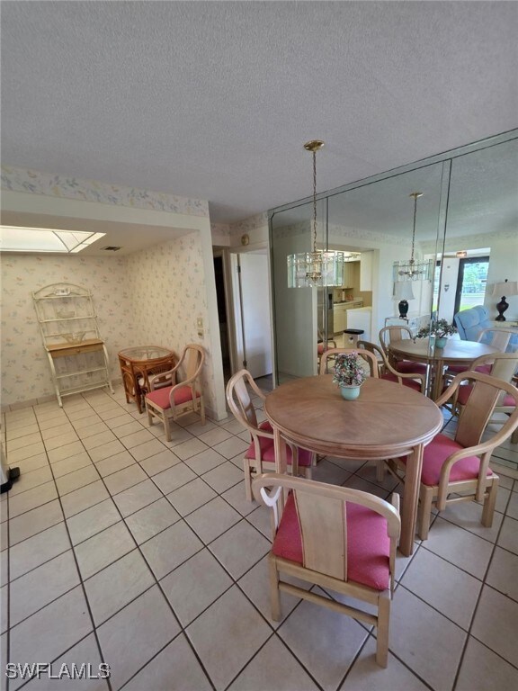 Dining space featuring wallpapered walls, light tile patterned floors, a textured ceiling, and a chandelier