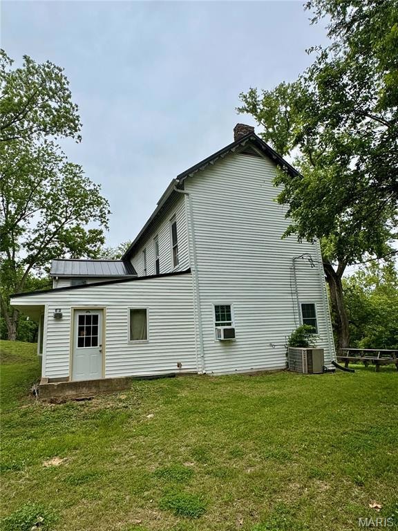 Rear view of property featuring a chimney, cooling unit, a lawn, and metal roof