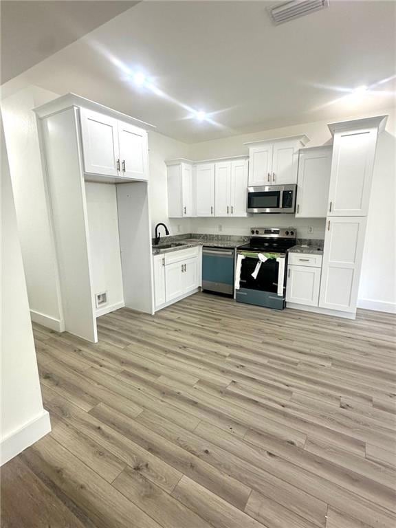 Kitchen featuring appliances with stainless steel finishes, white cabinets, light wood-type flooring, and dark stone counters