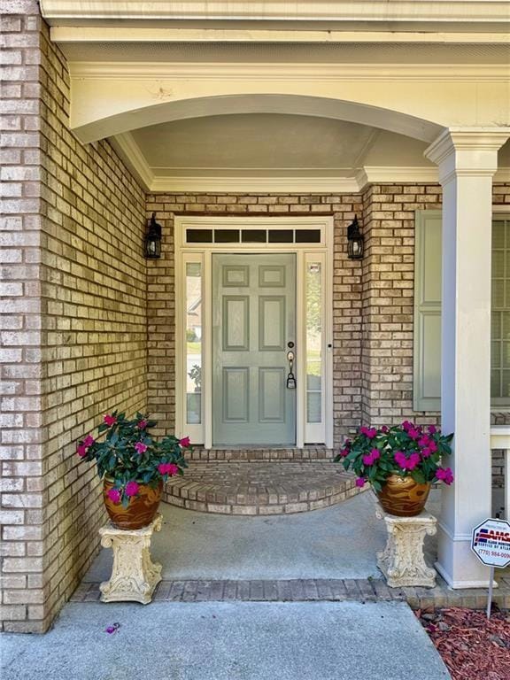 View of exterior entry featuring brick siding and a porch