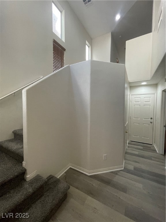 Staircase featuring wood finished floors, a high ceiling, and recessed lighting