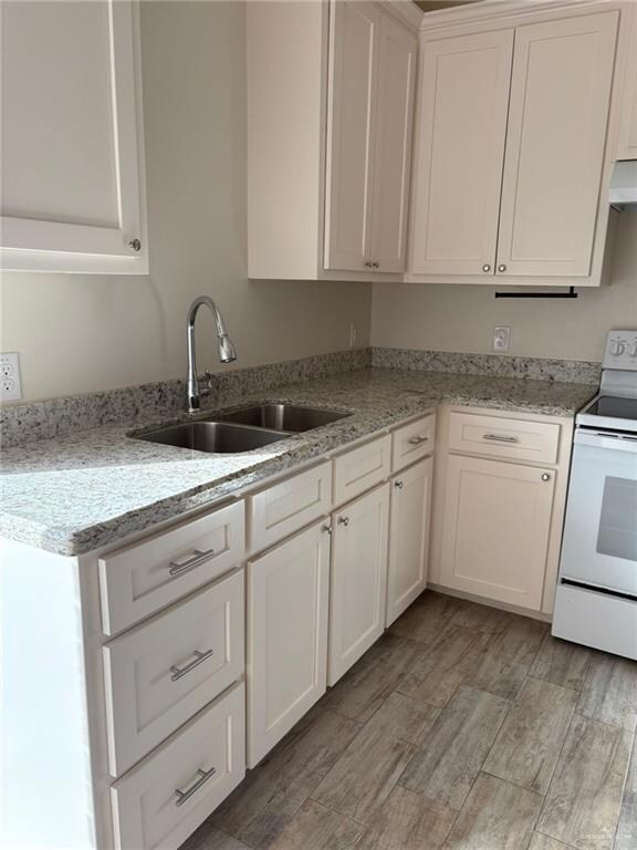 Kitchen featuring white cabinets, white range with electric cooktop, light stone countertops, under cabinet range hood, and light wood-style floors