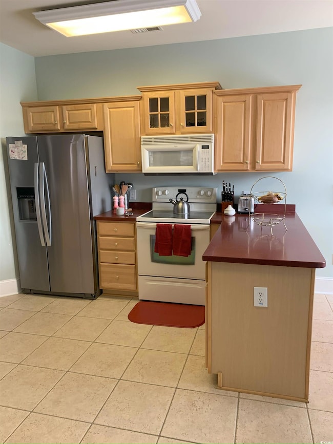 Kitchen featuring light tile patterned floors, white appliances, and kitchen peninsula