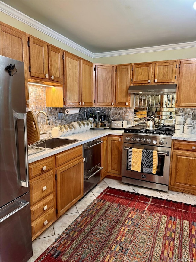 Kitchen featuring decorative backsplash, ornamental molding, light countertops, light tile patterned floors, and premium appliances