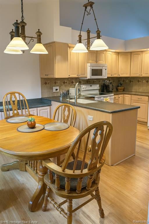 Kitchen with pendant lighting, white appliances, decorative backsplash, light wood-type flooring, and dark stone counters