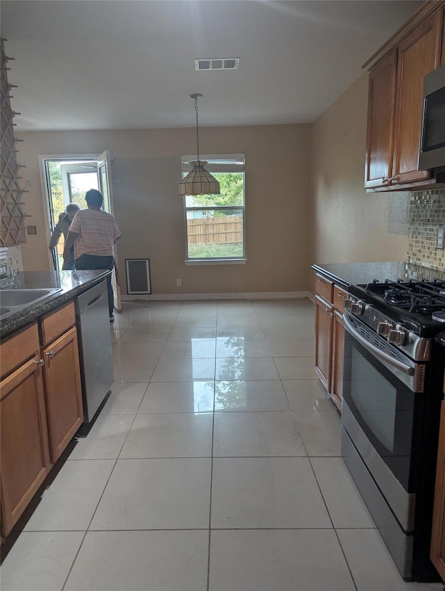 Kitchen with appliances with stainless steel finishes, brown cabinets, tasteful backsplash, and dark stone countertops