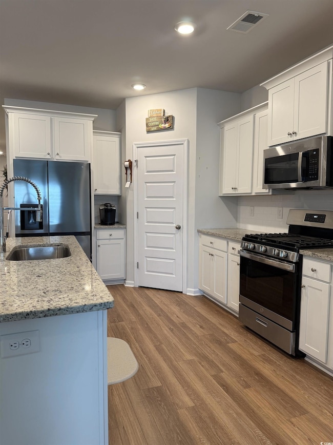 Kitchen featuring appliances with stainless steel finishes, wood finished floors, white cabinetry, light stone countertops, and recessed lighting