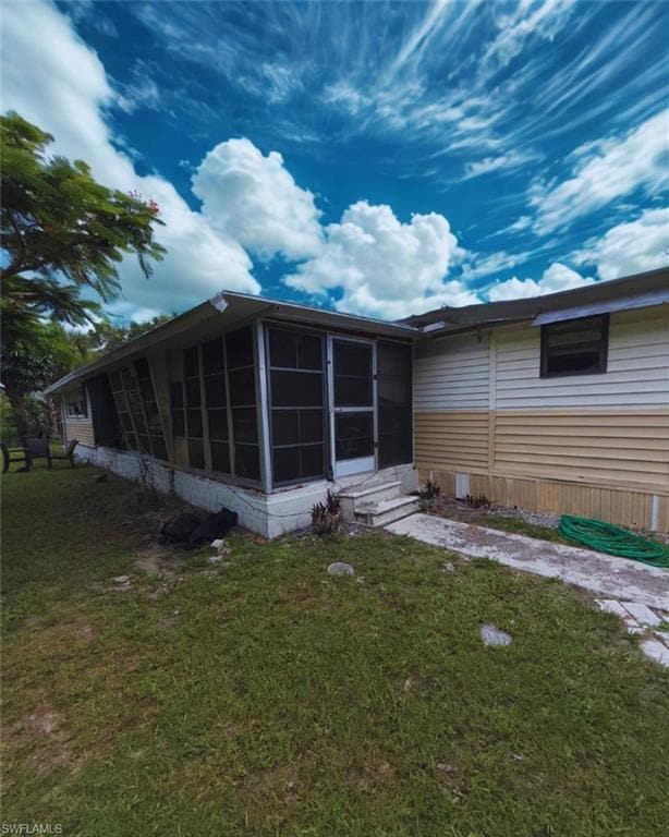 Back of property featuring a sunroom, a lawn, and entry steps