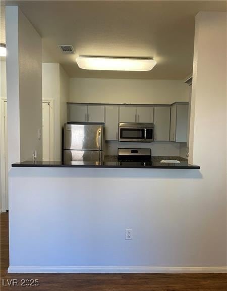 Kitchen featuring gray cabinetry, appliances with stainless steel finishes, dark wood finished floors, and a peninsula