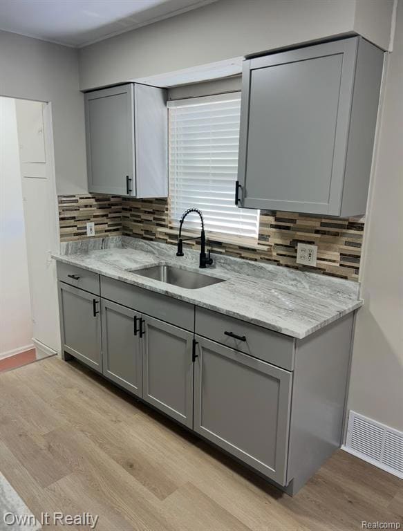 Kitchen featuring gray cabinets, light wood-type flooring, light stone counters, and decorative backsplash