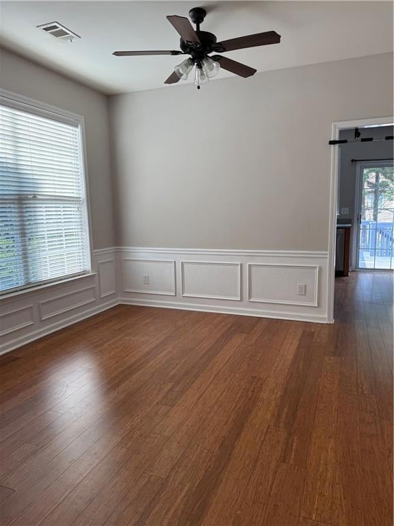 Spare room featuring dark wood-type flooring, a ceiling fan, wainscoting, and a decorative wall