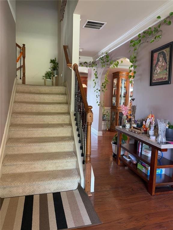 Stairs with ornamental molding, wood finished floors, and arched walkways