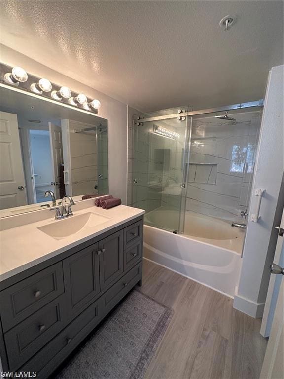 Bathroom featuring a textured ceiling, shower / bath combination with glass door, vanity, and light wood-style floors