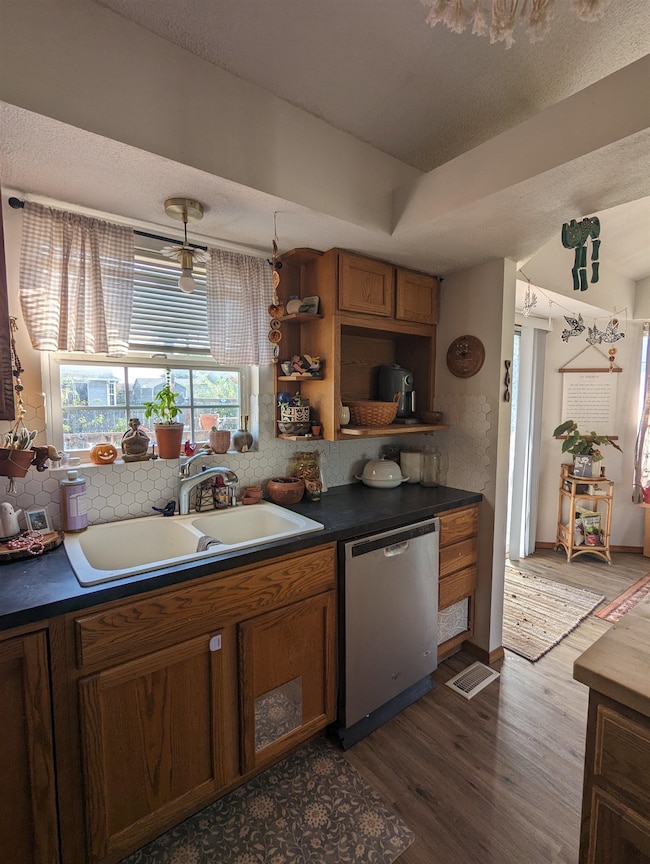 Kitchen with pendant lighting, dark wood-type flooring, sink, stainless steel dishwasher, and a textured ceiling