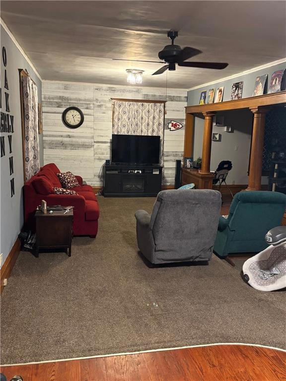 Living area featuring a ceiling fan, decorative columns, ornamental molding, wooden walls, and baseboards