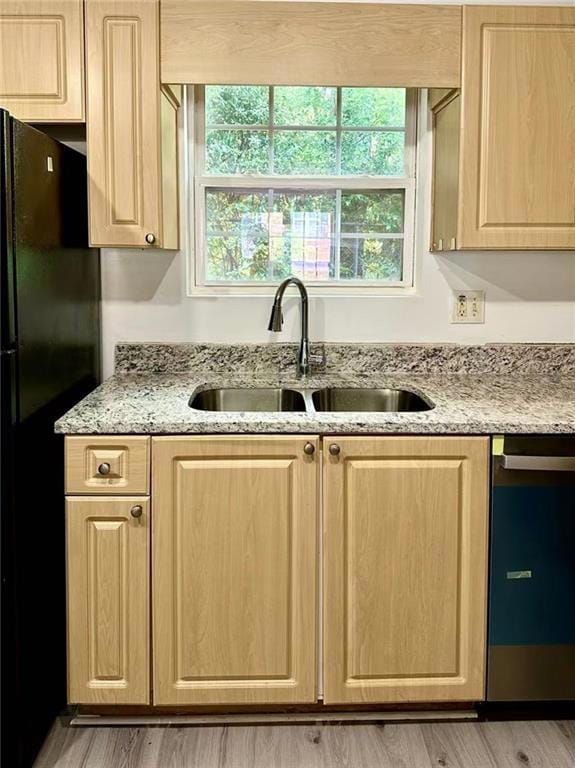 Kitchen with light brown cabinets, freestanding refrigerator, dishwasher, and light stone countertops