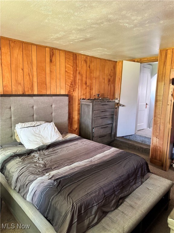 Bedroom featuring a textured ceiling, carpet flooring, and wooden walls