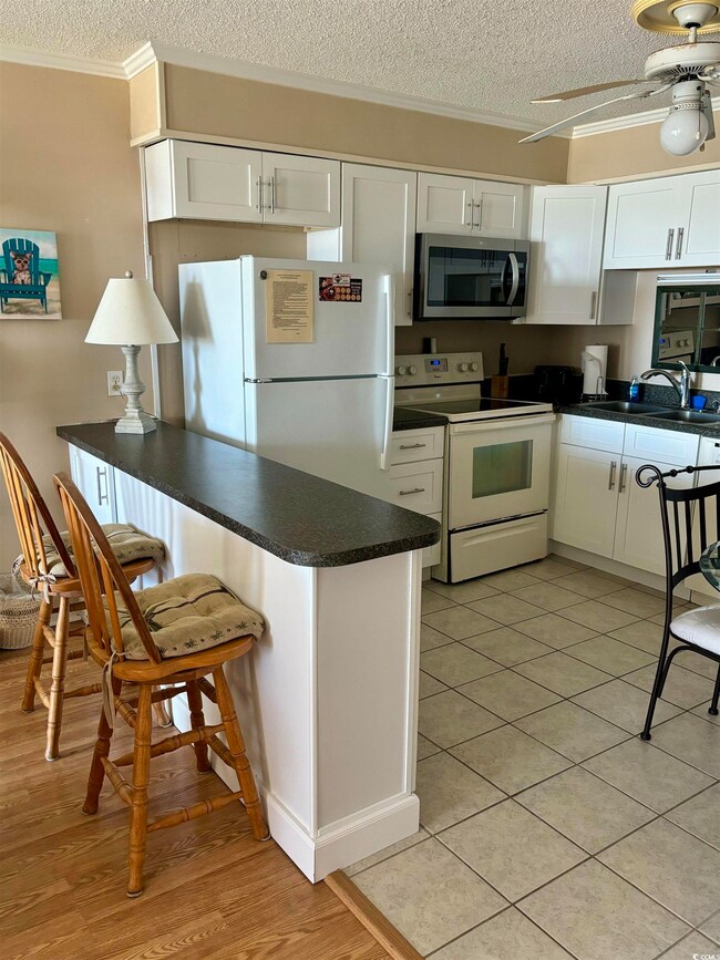 Kitchen with white appliances, a textured ceiling, and white cabinetry