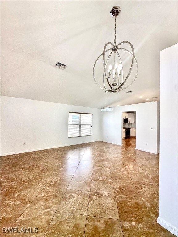 Spare room featuring a chandelier, vaulted ceiling