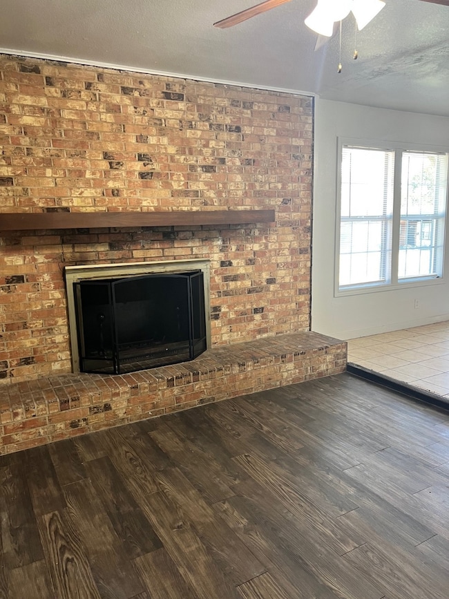 Detailed view of a brick fireplace, a textured ceiling, wood finished floors, and ceiling fan