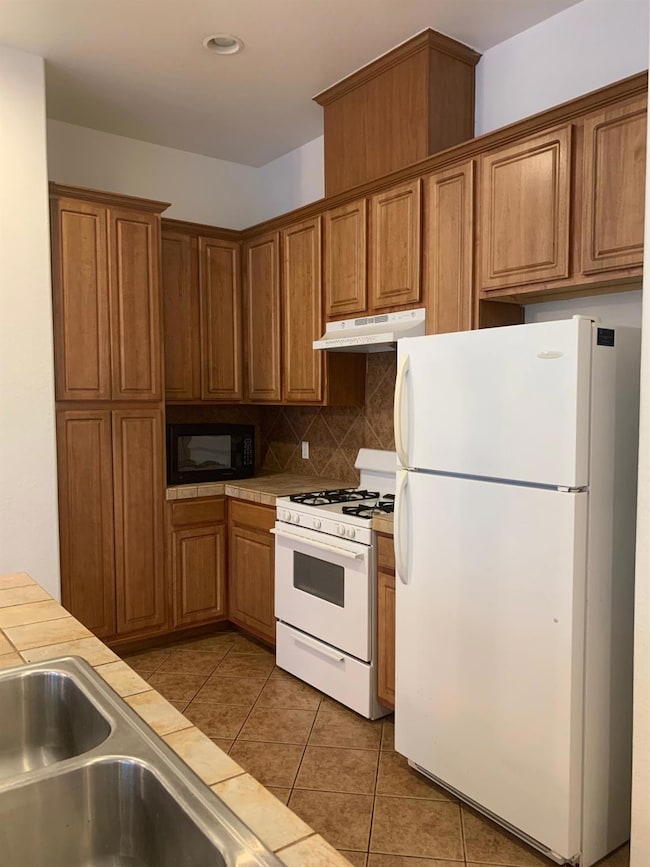 Kitchen with tile countertops, brown cabinetry, u