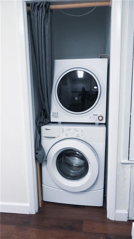 Washroom featuring dark wood-style floors and stacked washing machine and dryer