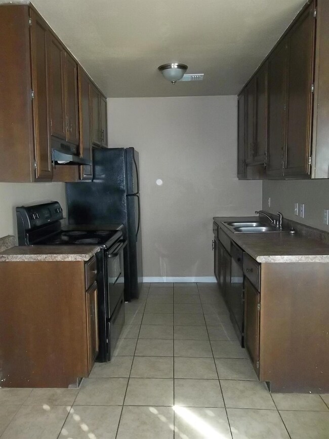 Kitchen with light tile patterned floors, sink, range, dark brown cabinetry, and exhaust hood