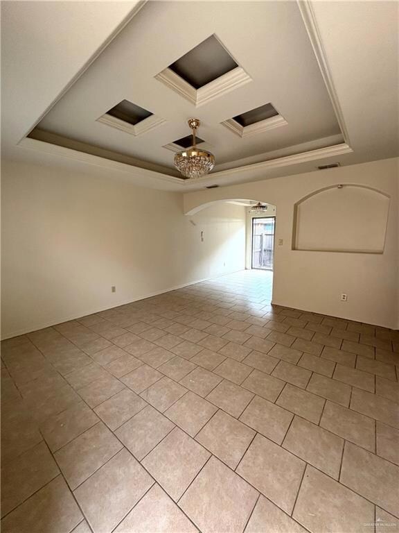 Unfurnished room with a tray ceiling, light tile patterned floors, visible vents, crown molding, and arched walkways