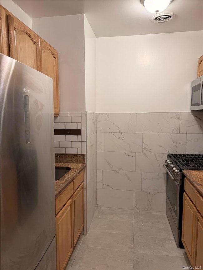 Kitchen featuring stainless steel appliances, dark stone counters, tile walls, light brown cabinets, and light tile patterned floors