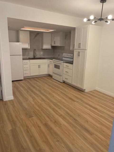 Kitchen with white appliances, a chandelier, light wood-type flooring, decorative backsplash, and sink