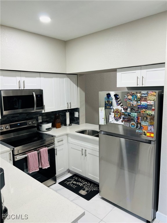 Kitchen featuring stainless steel appliances, white cabinets, a textured wall, light stone countertops, and light tile patterned floors