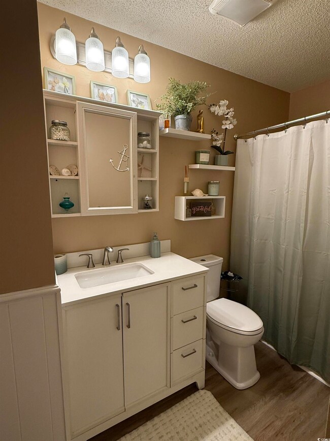 Bathroom with vanity, a shower with curtain, light wood-type flooring, and a textured ceiling