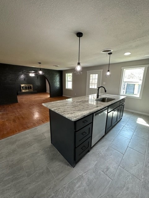 Kitchen featuring hanging light fixtures, a kitchen island with sink, light stone counters, open floor plan, and a textured ceiling