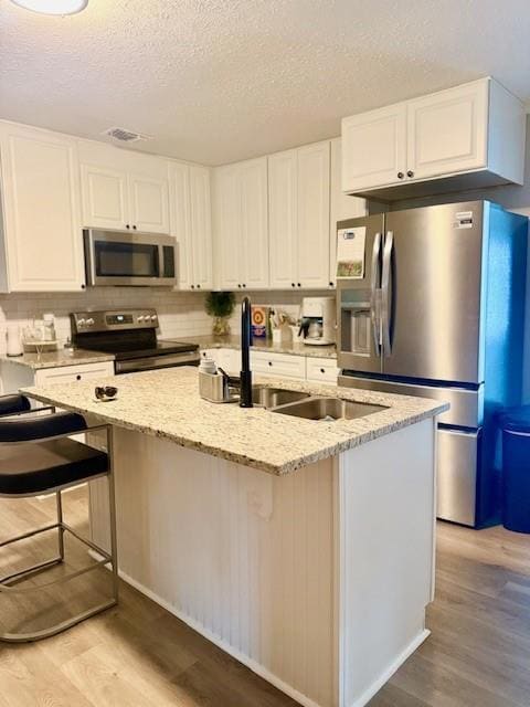 Kitchen featuring appliances with stainless steel finishes, light wood-style flooring, white cabinets, light stone counters, and a textured ceiling