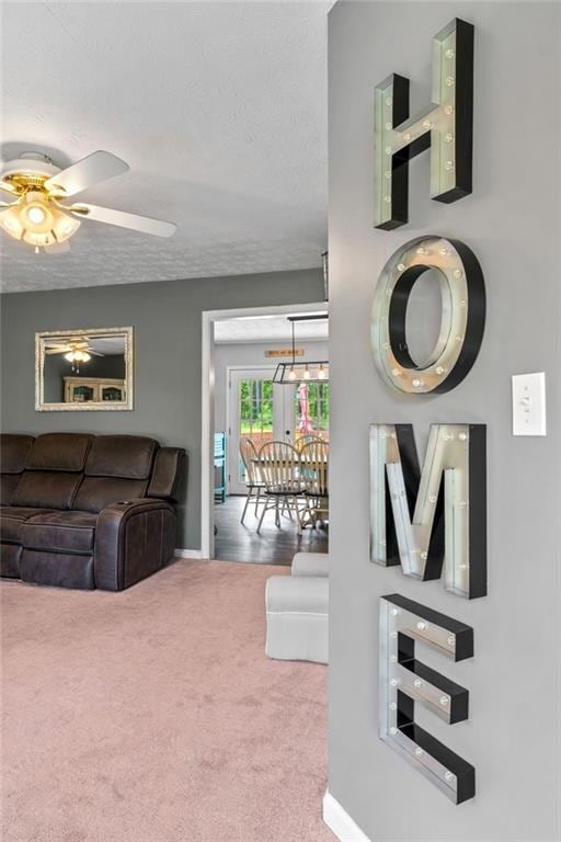 Carpeted living area featuring baseboards, a ceiling fan, and a textured ceiling