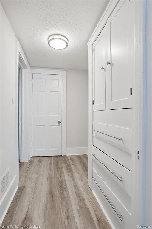 Hall with a textured ceiling and light wood finished floors