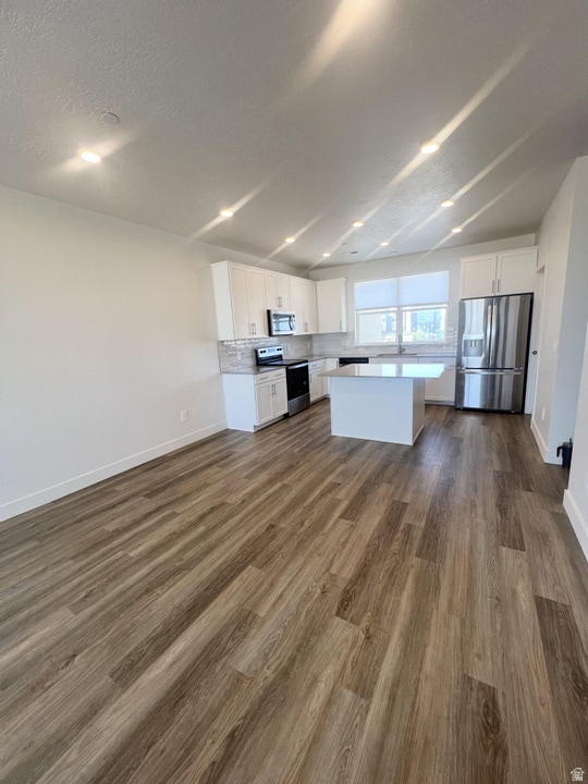 Kitchen featuring white cabinetry, appliances with stainless steel finishes, open floor plan, dark wood-style floors, and a kitchen island