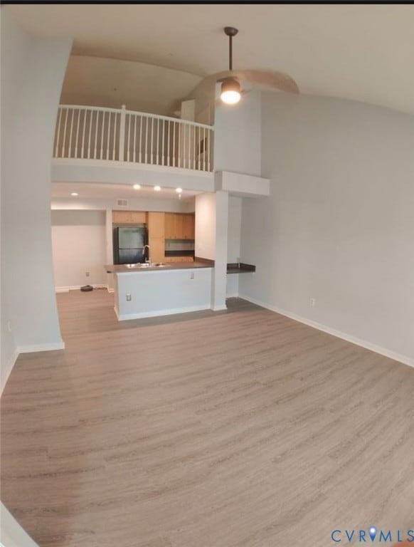 Unfurnished living room with light wood-style floors, high vaulted ceiling, and ceiling fan