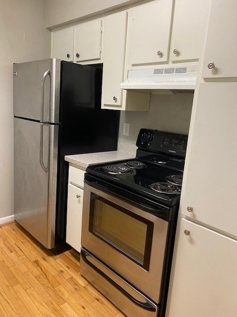This kitchen has stainless steel appliances, including a refrigerator and stove. It features white cabinetry and laminate flooring, offering a clean and functional space.
