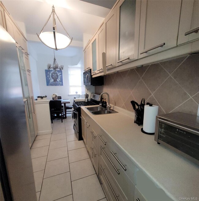 Kitchen with decorative backsplash, appliances with stainless steel finishes, light tile patterned flooring, light countertops, and a chandelier