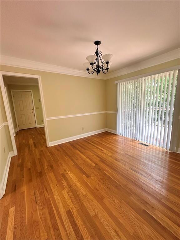 Unfurnished room featuring a chandelier, baseboards, crown molding, and wood finished floors