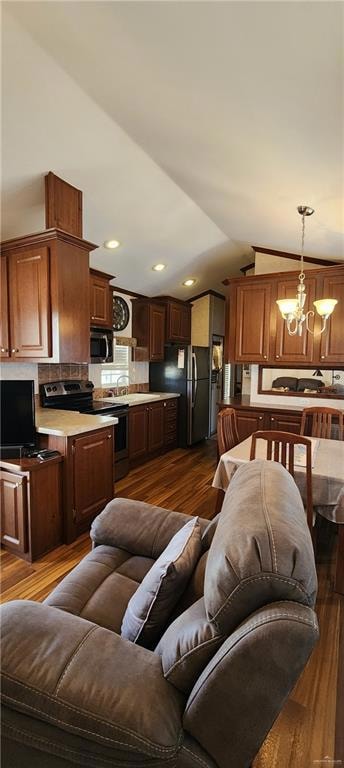 Living area featuring dark wood-style floors, a chandelier, vaulted ceiling, and recessed lighting