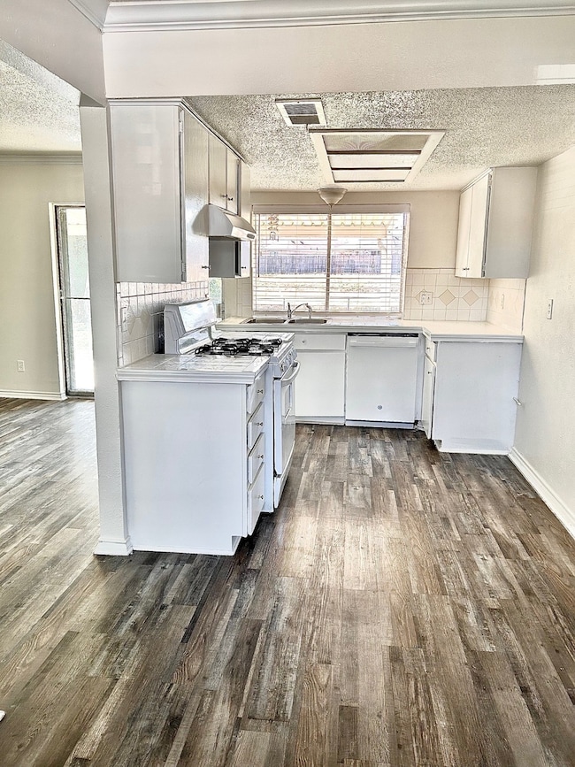 Kitchen with white cabinets, white appliances, light countertops, tasteful backsplash, and dark wood-style flooring