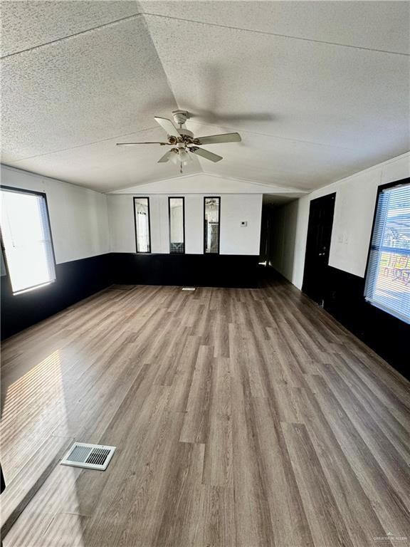 Empty room featuring light hardwood / wood-style floors, ceiling fan, a textured ceiling, and lofted ceiling