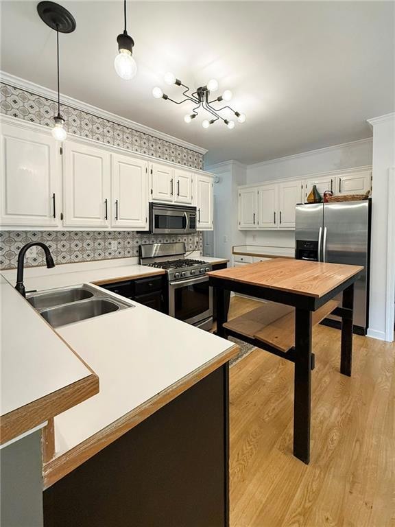 Kitchen with appliances with stainless steel finishes, crown molding, white cabinets, light wood finished floors, and light countertops
