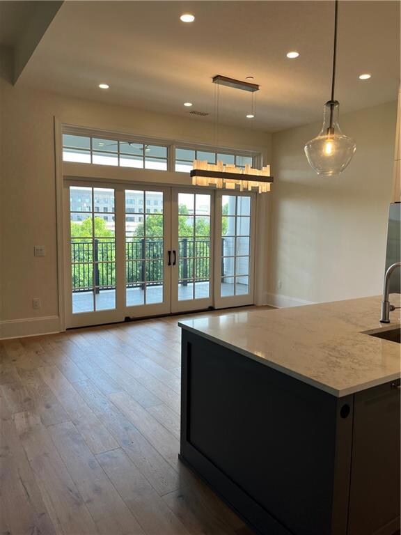 Kitchen with pendant lighting, recessed lighting, light wood finished floors, dark cabinetry, and an island with sink