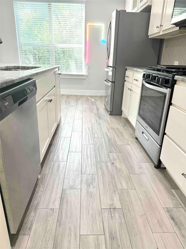 Kitchen with appliances with stainless steel finishes, wood finish floors, and white cabinets