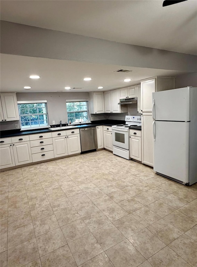 Kitchen with white appliances, dark countertops, white cabinetry, recessed lighting, and under cabinet range hood