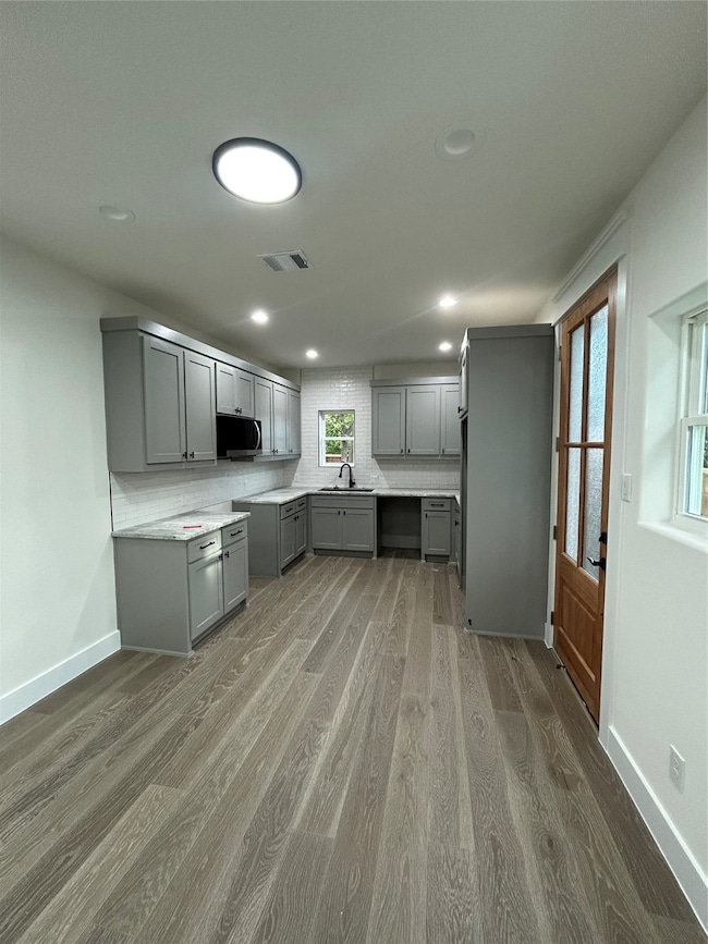 Kitchen featuring gray cabinetry, backsplash, light wood-style floors, recessed lighting, and light stone countertops